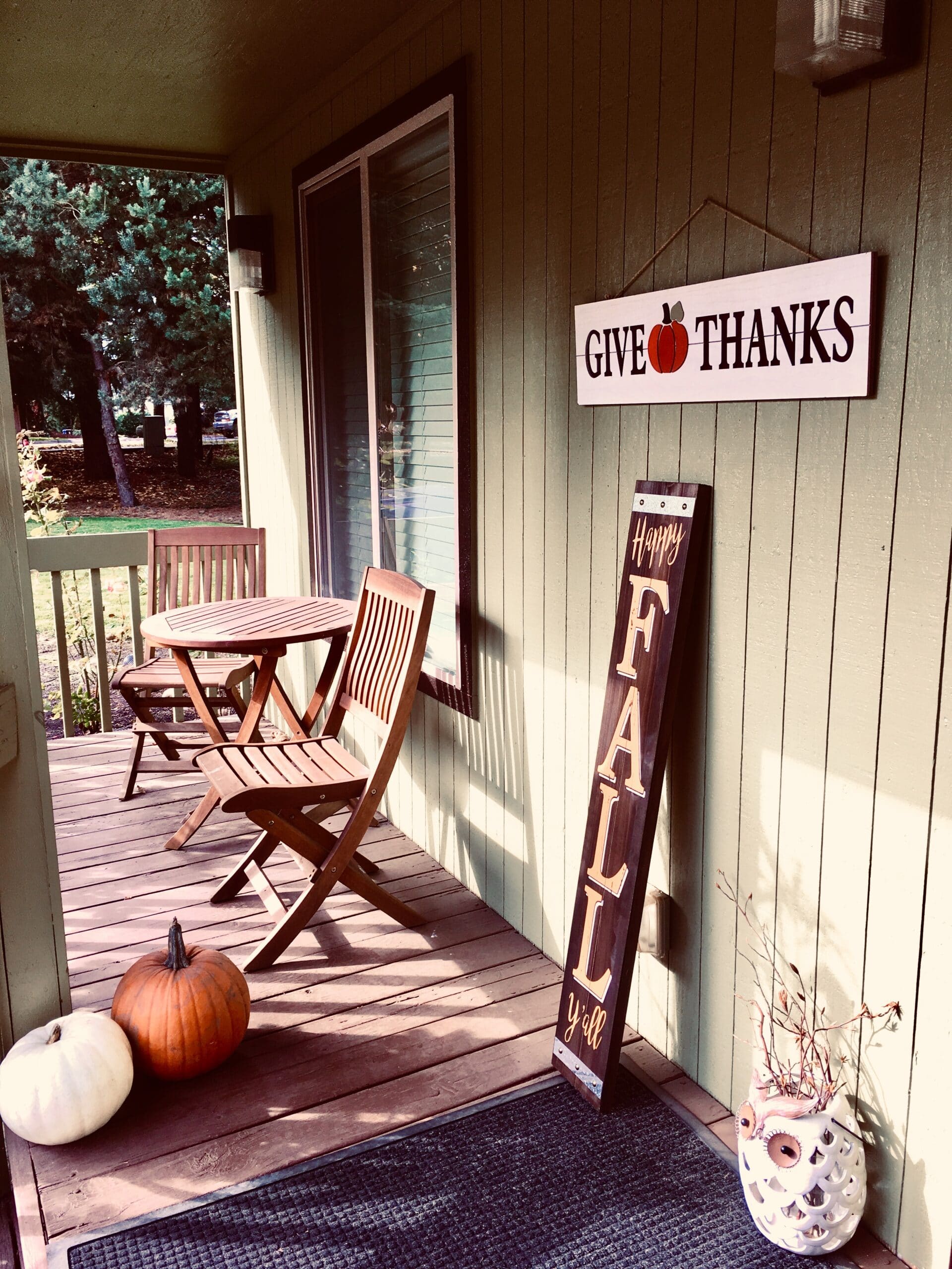 An image of a front porch with a small bistro table and folding chairs and fall decor.