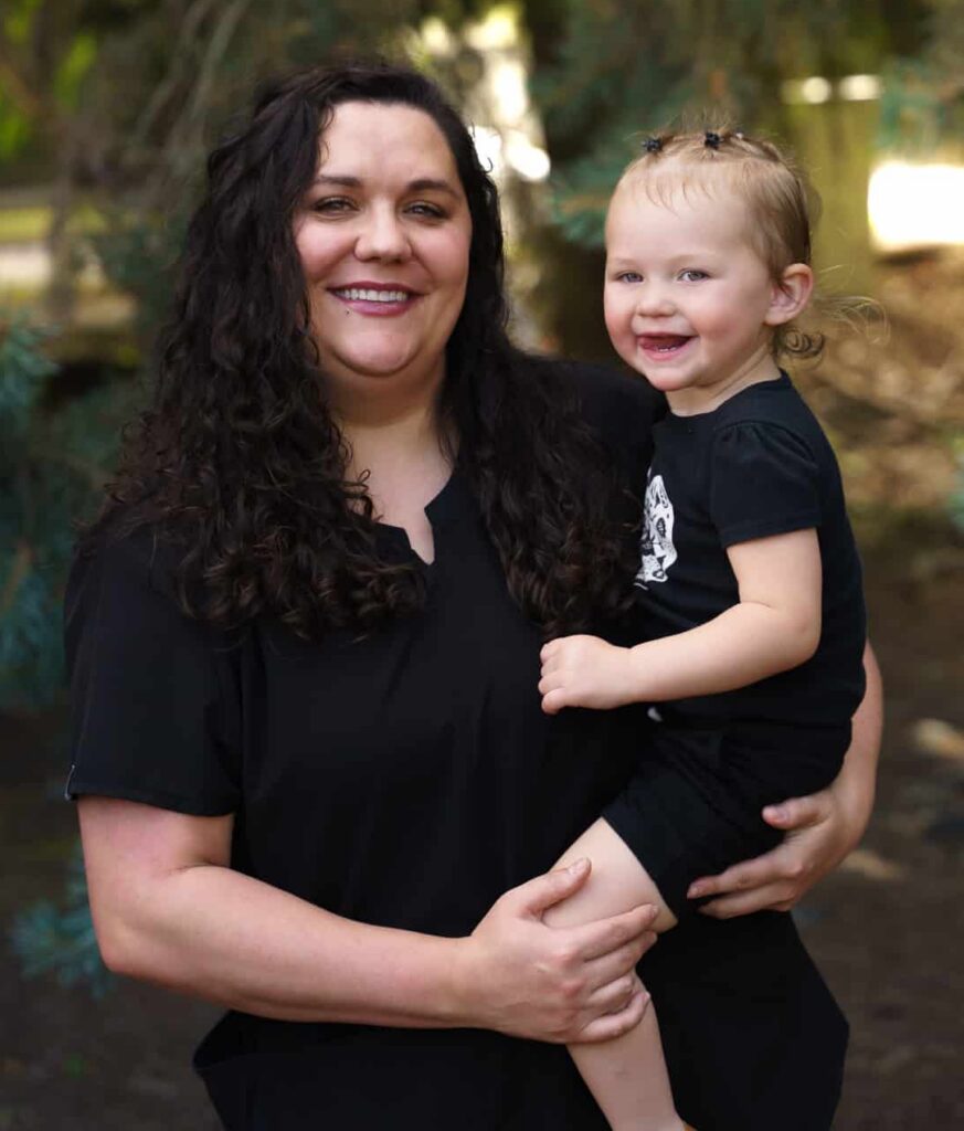 An image of Dr. Westbrook, a female chiropractor, smiling and holding her smiling toddler daughter.
