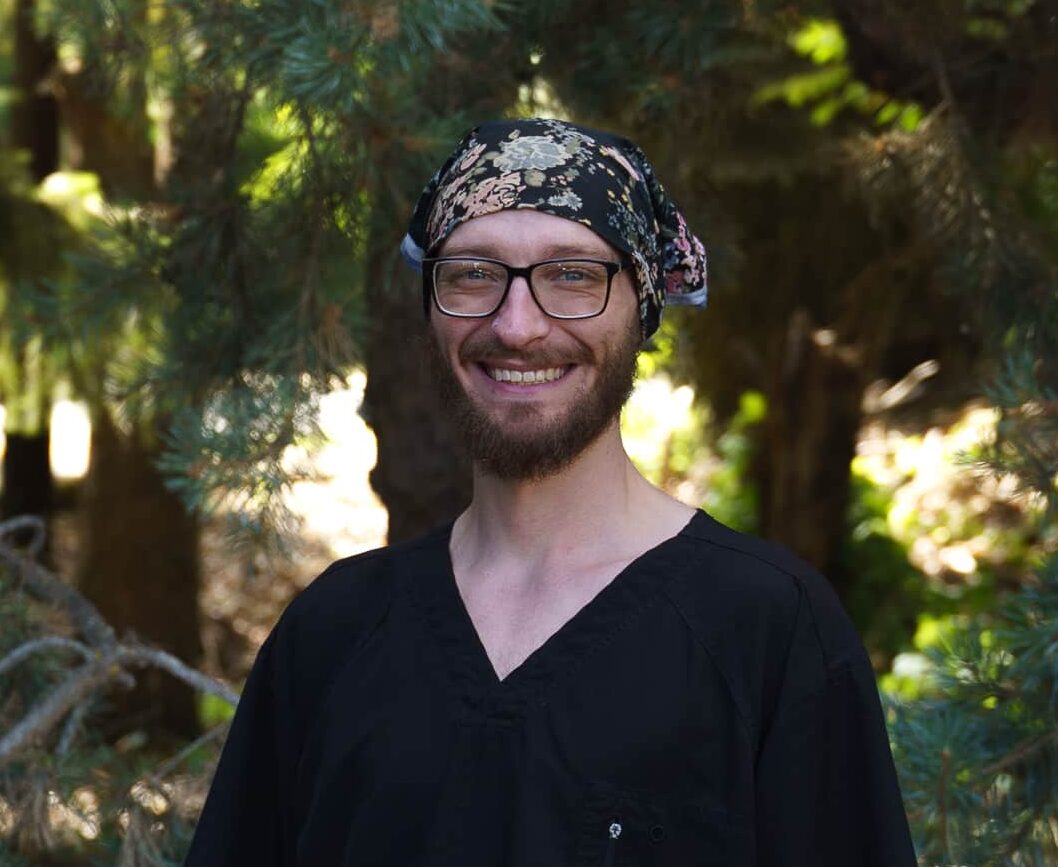 An image of a smiling man in scrubs, wearing glasses and a bandana.
