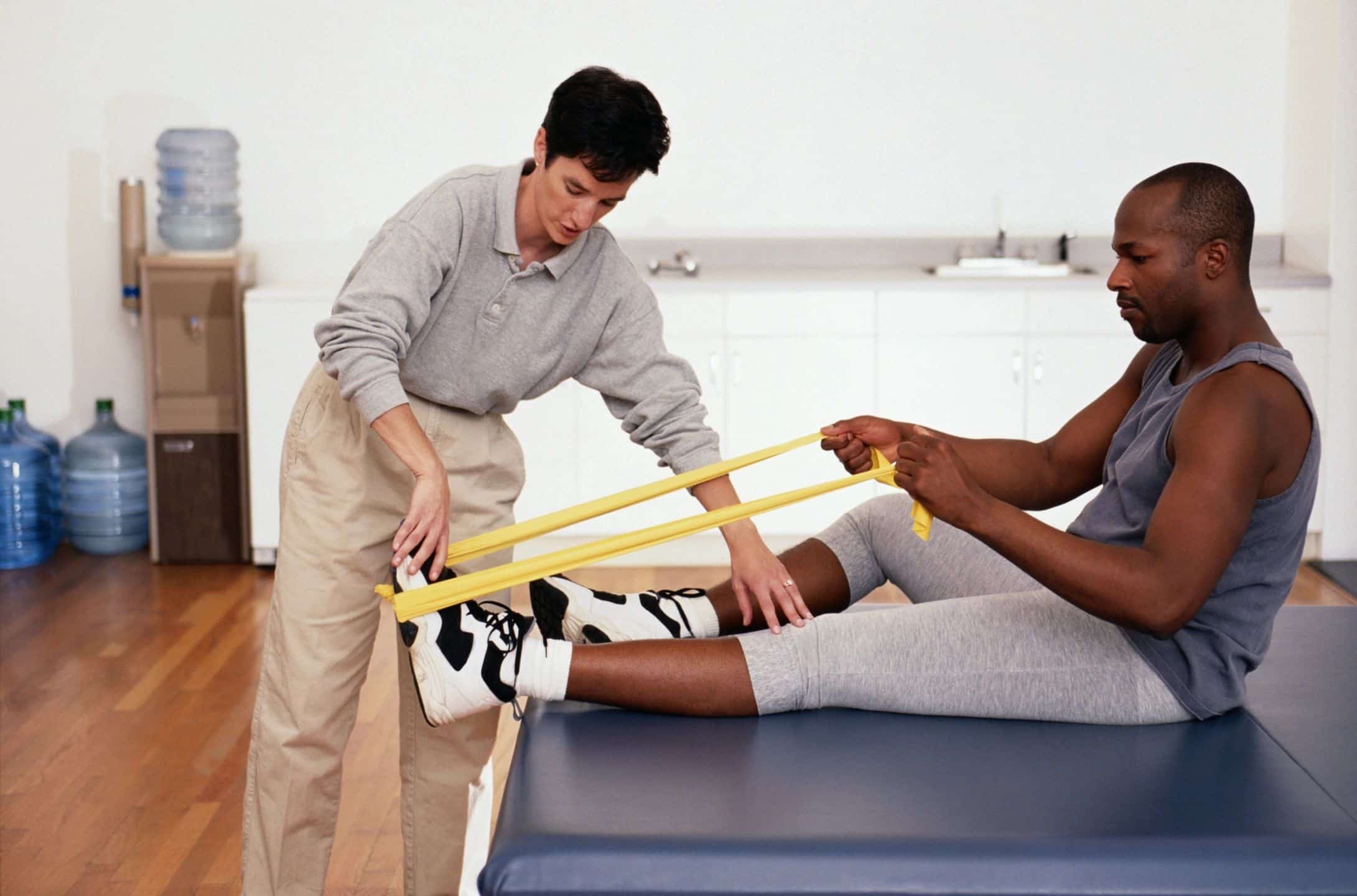 A male patient using resistance bands with the help of a physical therapist