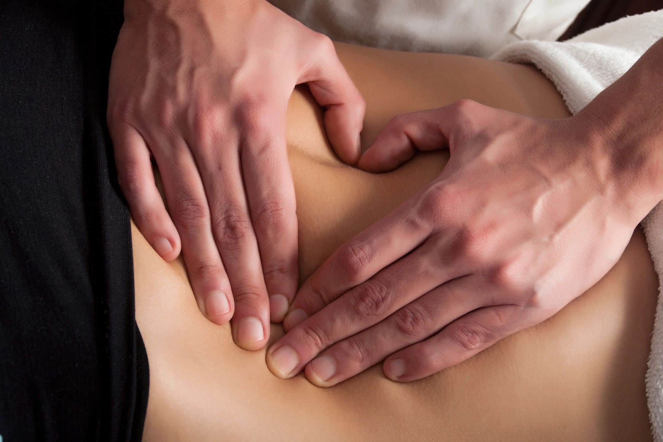 An image of a patient laying on their stomach with a chiropractor pressing on their back, with their thumbs and first fingers arranged to make a heart.