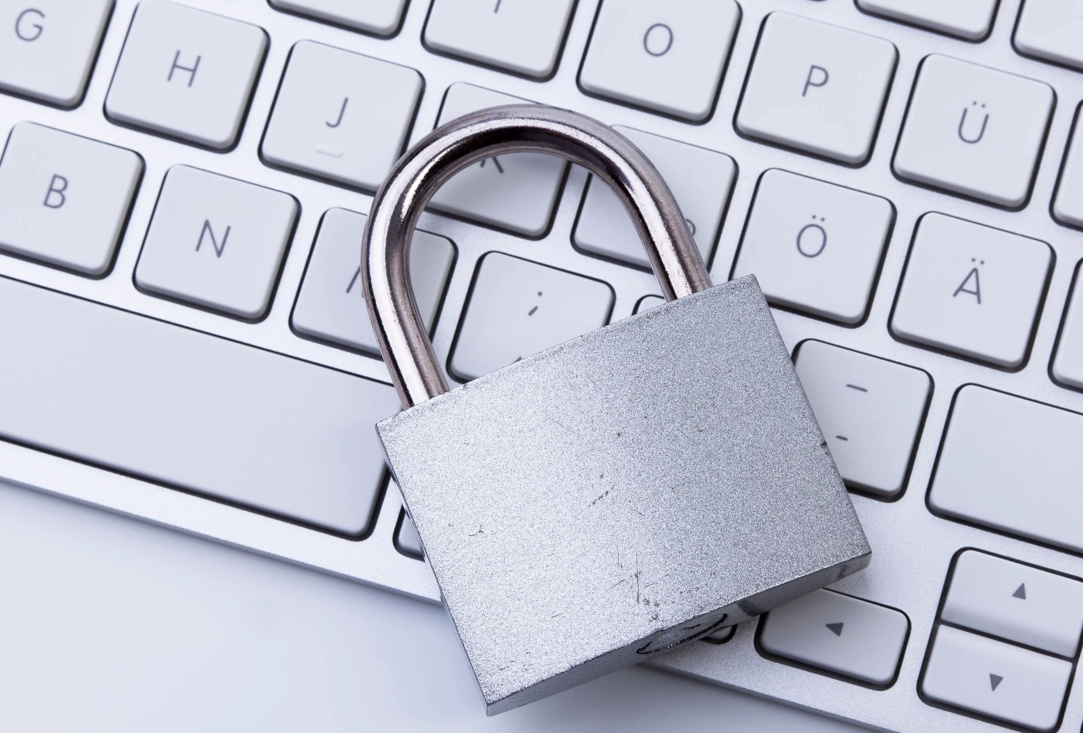 An image of a silver padlock resting on top of a white computer keyboard.