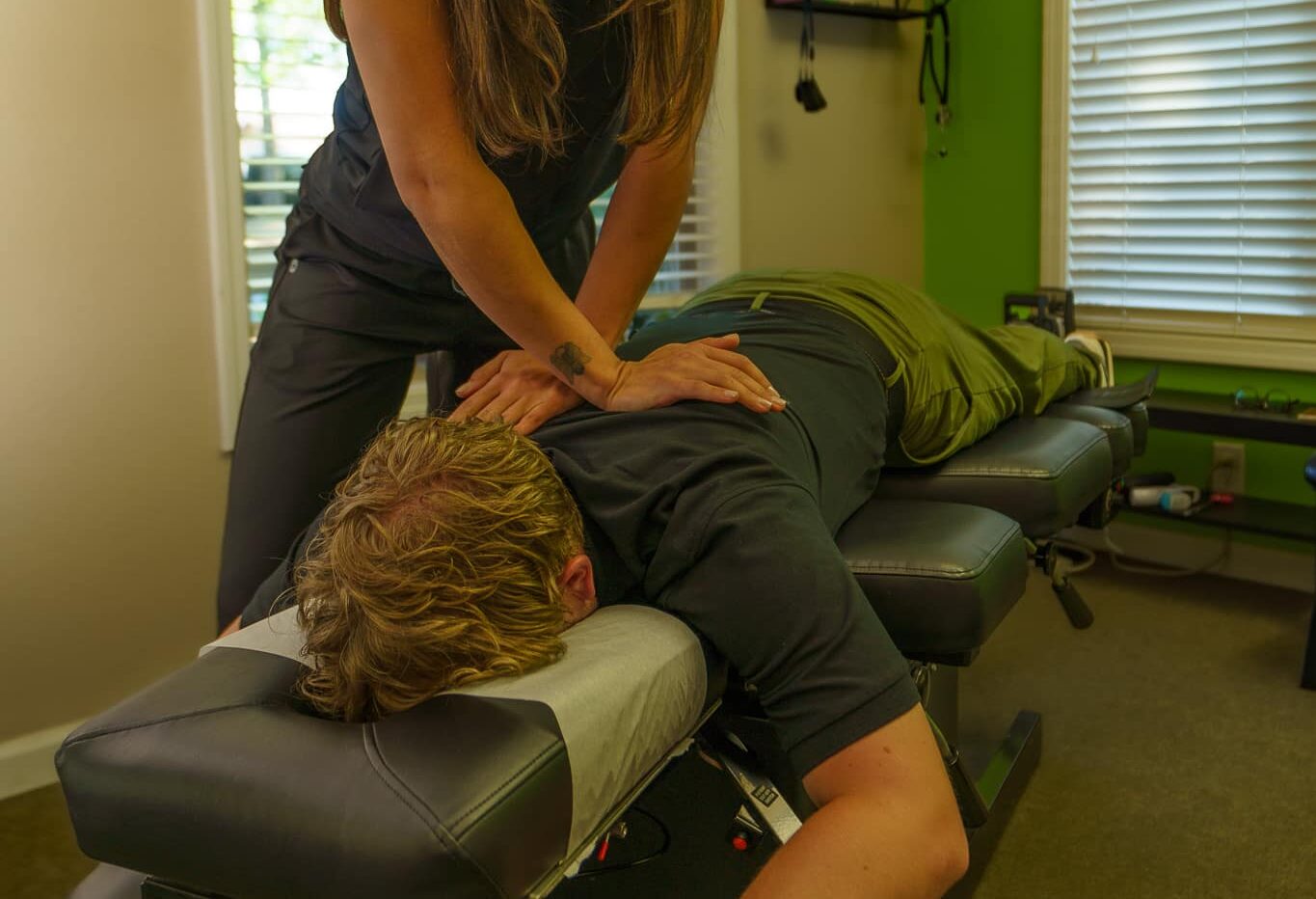 An image of a male patient laying face-down on a chiropractic table receiving an adjustment from a female chiropractor.